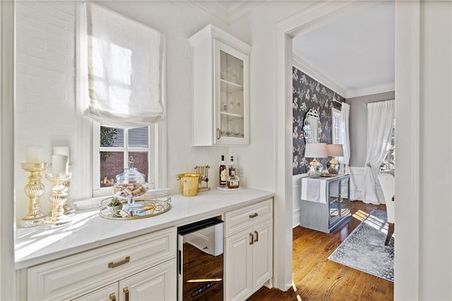 bar with wine cooler, light stone counters, ornamental molding, wood-type flooring, and white cabinetry