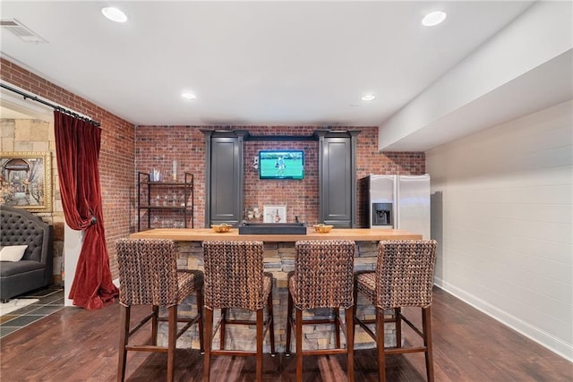 bar featuring butcher block countertops, stainless steel fridge with ice dispenser, brick wall, and dark hardwood / wood-style floors