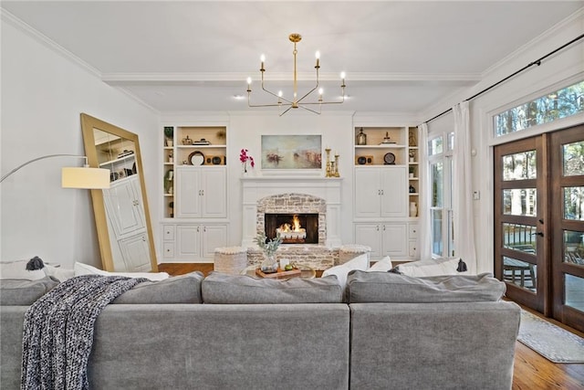 living room featuring french doors, a brick fireplace, built in features, light hardwood / wood-style floors, and a chandelier