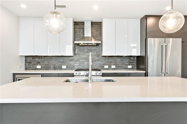 kitchen with high end refrigerator, pendant lighting, wall chimney range hood, and white cabinets