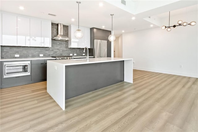 kitchen with hanging light fixtures, wall chimney exhaust hood, light hardwood / wood-style flooring, appliances with stainless steel finishes, and a center island