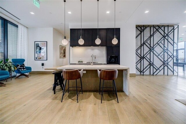 kitchen with sink, a center island with sink, decorative light fixtures, a kitchen breakfast bar, and light hardwood / wood-style floors