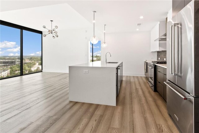 kitchen featuring an island with sink, white cabinets, appliances with stainless steel finishes, and hanging light fixtures