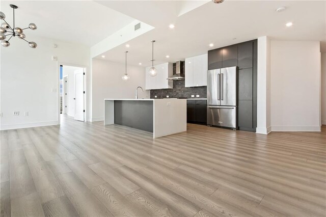 kitchen featuring a kitchen island with sink, hanging light fixtures, high quality fridge, light hardwood / wood-style flooring, and wall chimney exhaust hood