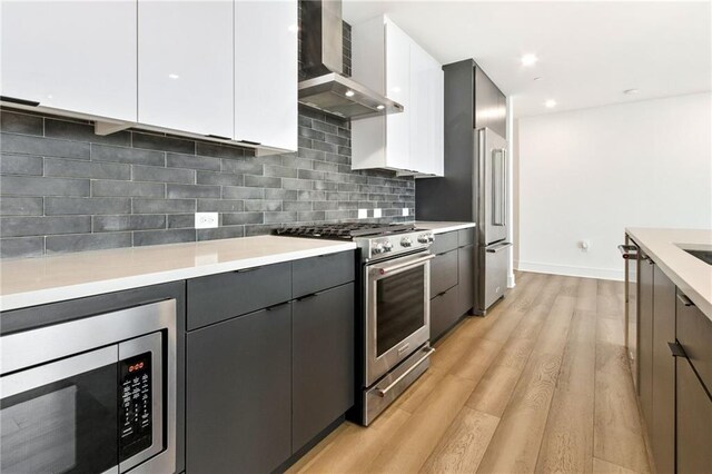 kitchen featuring light hardwood / wood-style floors, white cabinets, backsplash, high end appliances, and wall chimney range hood