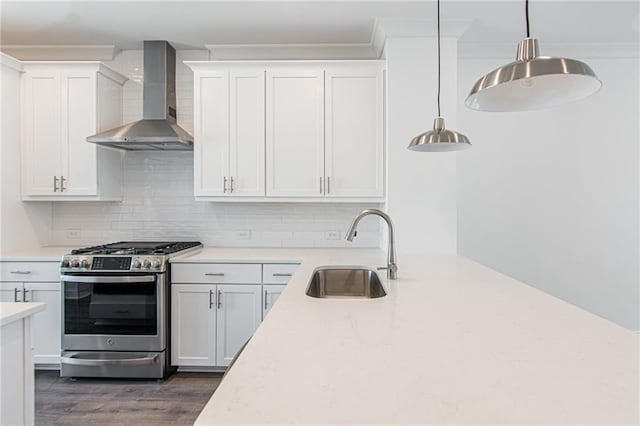 kitchen featuring a sink, light countertops, wall chimney range hood, stainless steel gas stove, and dark wood finished floors