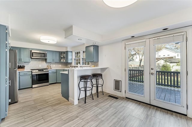 kitchen featuring appliances with stainless steel finishes, a breakfast bar area, a peninsula, light countertops, and backsplash