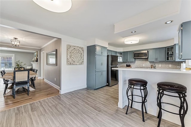 kitchen featuring light countertops, stainless steel microwave, decorative backsplash, freestanding refrigerator, and a peninsula