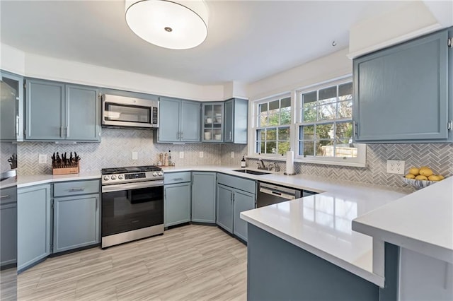 kitchen featuring light countertops, backsplash, appliances with stainless steel finishes, glass insert cabinets, and a peninsula