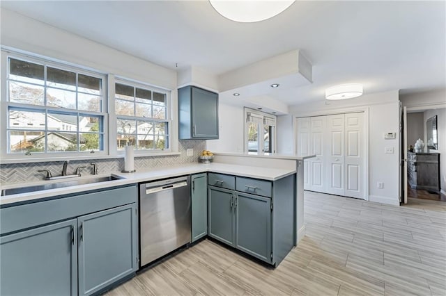 kitchen with light countertops, decorative backsplash, stainless steel dishwasher, a sink, and a peninsula