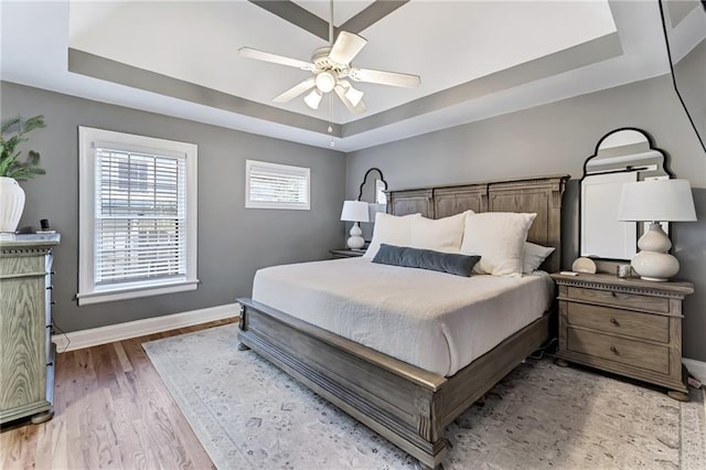 bedroom with wood finished floors, a raised ceiling, a ceiling fan, and baseboards