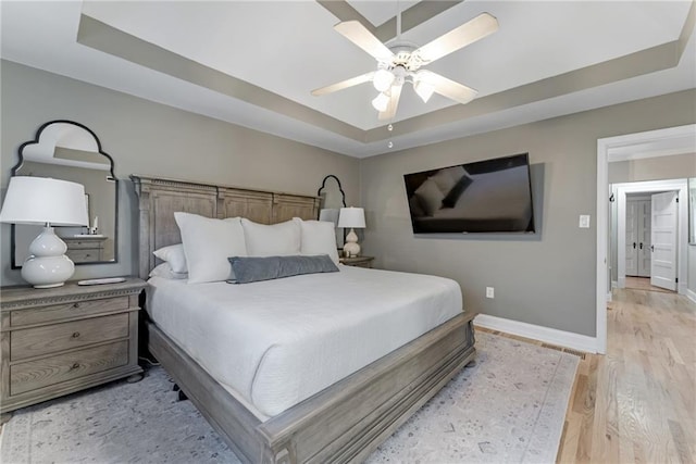 bedroom with a ceiling fan, a tray ceiling, baseboards, and light wood finished floors