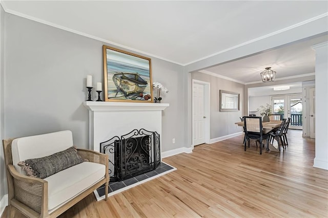 sitting room featuring light wood finished floors, baseboards, a fireplace with raised hearth, and crown molding