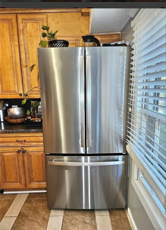 kitchen featuring stainless steel refrigerator, dark tile patterned floors, and dark stone counters