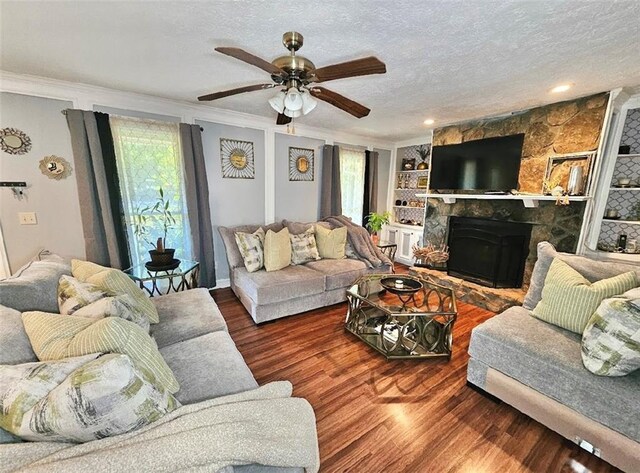 living room featuring ornamental molding, a textured ceiling, dark hardwood / wood-style flooring, ceiling fan, and a stone fireplace