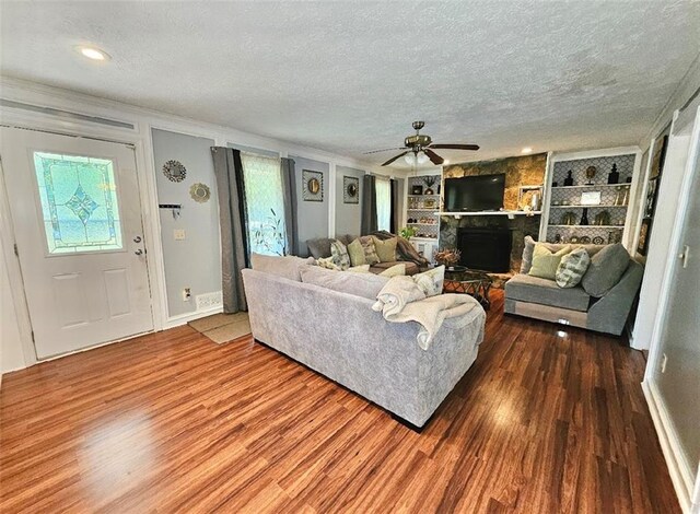 living room featuring built in features, hardwood / wood-style flooring, ceiling fan, and a stone fireplace