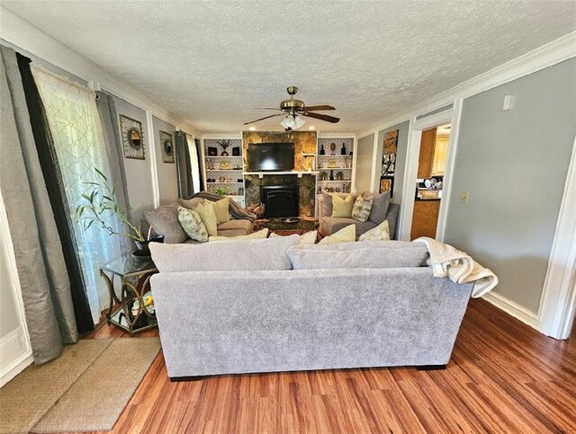 living room with a textured ceiling, wood-type flooring, built in features, ornamental molding, and ceiling fan