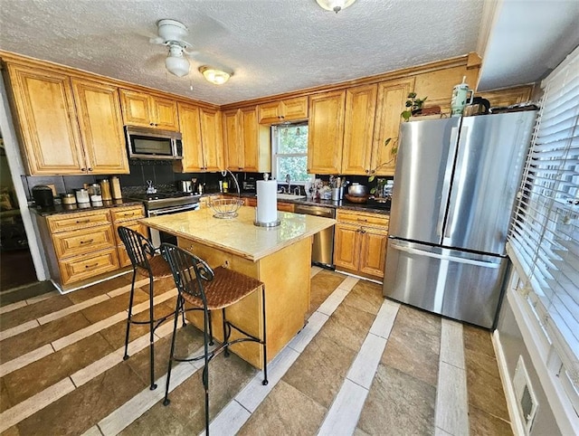 kitchen with a textured ceiling, a kitchen island, light tile patterned floors, appliances with stainless steel finishes, and ceiling fan