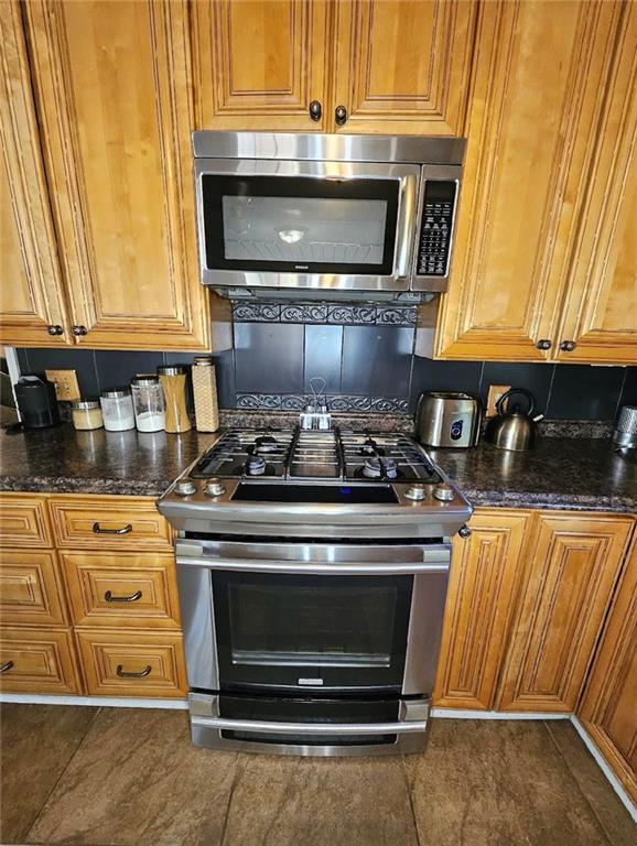 kitchen with dark stone countertops, dark tile patterned flooring, and stainless steel appliances