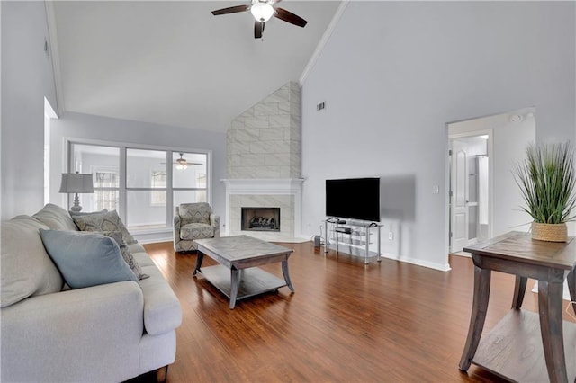 living area featuring high vaulted ceiling, ceiling fan, a tiled fireplace, and wood finished floors