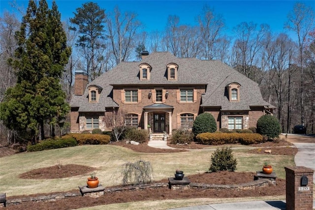 view of front facade with brick siding, a chimney, and a front yard