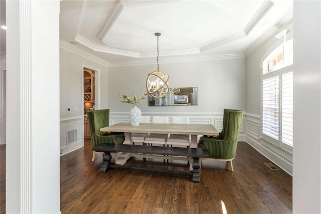dining space with dark wood-style flooring, a chandelier, wainscoting, a tray ceiling, and ornamental molding