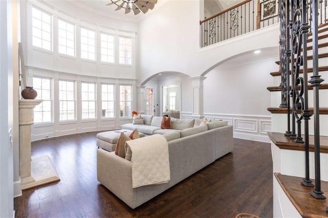 living area with arched walkways, crown molding, a high ceiling, ornate columns, and healthy amount of natural light