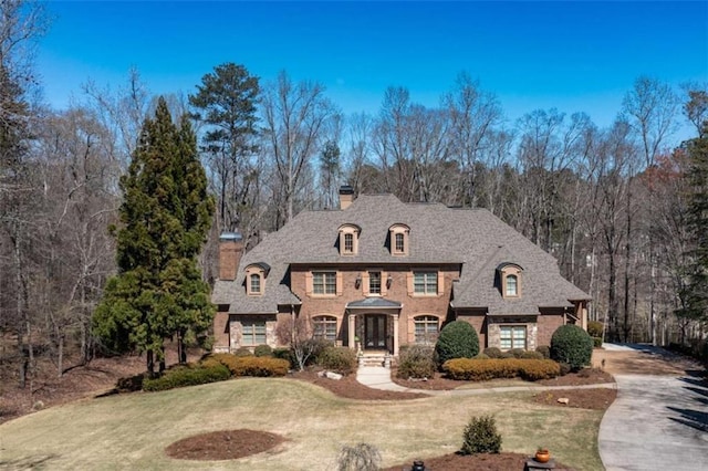 french country style house featuring a chimney, a front yard, brick siding, and concrete driveway