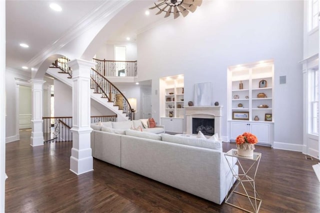 living room featuring arched walkways, crown molding, stairs, built in shelves, and dark wood finished floors