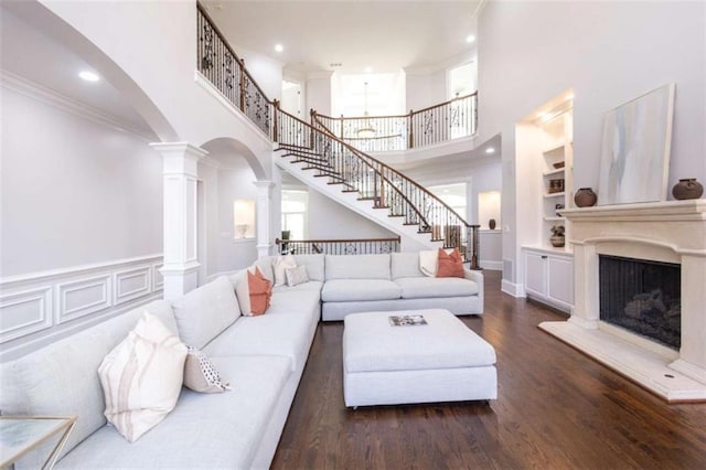 living area with ornate columns, arched walkways, a towering ceiling, stairway, and crown molding