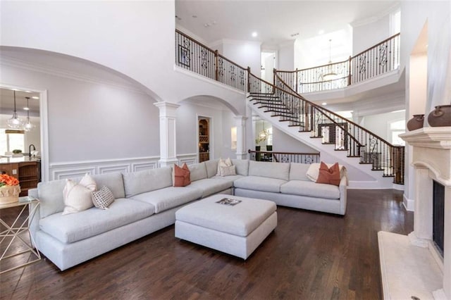 living room with ornate columns, arched walkways, a high ceiling, stairway, and a fireplace