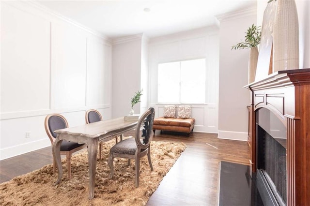 dining space with a decorative wall, a fireplace with flush hearth, wood finished floors, ornamental molding, and baseboards
