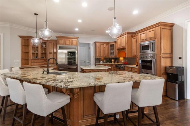 kitchen featuring built in appliances, brown cabinets, a large island with sink, a sink, and decorative backsplash