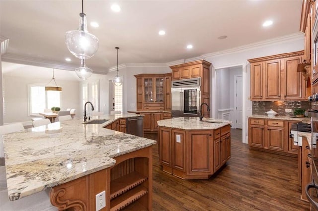 kitchen featuring stainless steel appliances, a large island, a sink, brown cabinetry, and ornamental molding