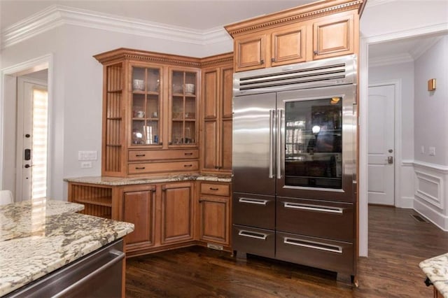 kitchen featuring built in refrigerator, dark wood-type flooring, brown cabinetry, and ornamental molding