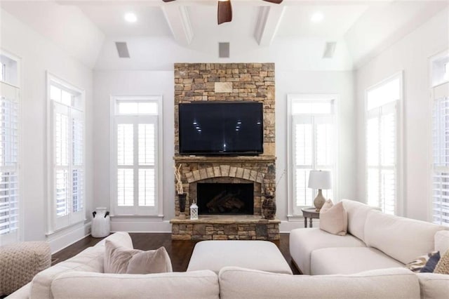 living area with wood finished floors, a ceiling fan, a stone fireplace, baseboards, and beam ceiling