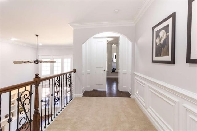 hallway with arched walkways, ornamental molding, wainscoting, a decorative wall, and carpet