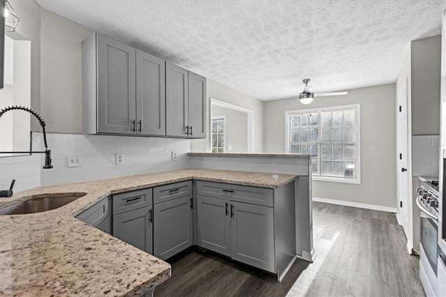 kitchen with sink, gray cabinets, backsplash, light stone counters, and kitchen peninsula