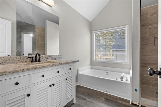 bathroom with lofted ceiling, hardwood / wood-style floors, vanity, and a tub