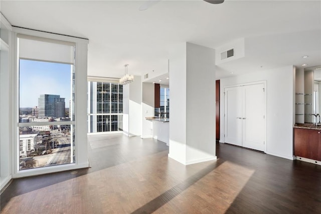 unfurnished living room featuring floor to ceiling windows, dark hardwood / wood-style floors, sink, and an inviting chandelier