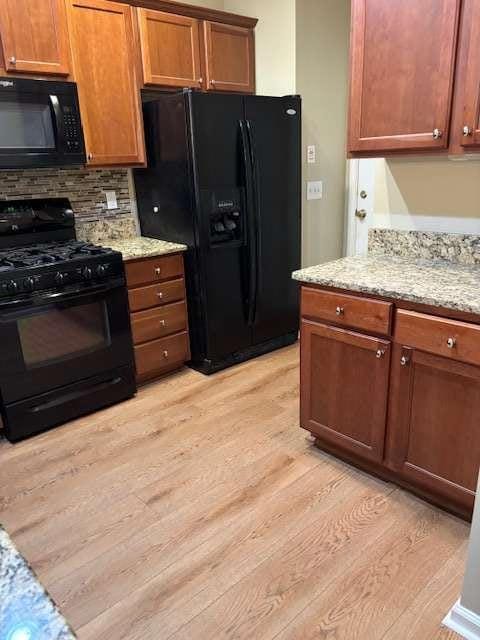 1629 Marsanne Ter, Kennesaw, GA 30152 - kitchen featuring black appliances, light wood-style floors, decorative backsplash, and light stone counters