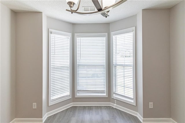249 Bainbridge Cir, Dallas, GA 30132 - empty room featuring wood finished floors, baseboards, visible vents, an inviting chandelier, and a textured ceiling