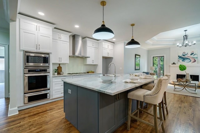 kitchen featuring appliances with stainless steel finishes, wall chimney range hood, white cabinets, hanging light fixtures, and a large island