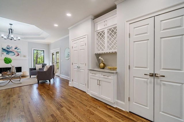 bar featuring crown molding, an inviting chandelier, light hardwood / wood-style flooring, white cabinetry, and hanging light fixtures