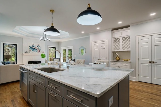 kitchen featuring a center island with sink, sink, hanging light fixtures, and a tray ceiling