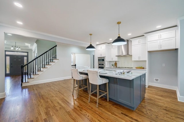 kitchen featuring stainless steel appliances, wall chimney range hood, white cabinets, hanging light fixtures, and a large island