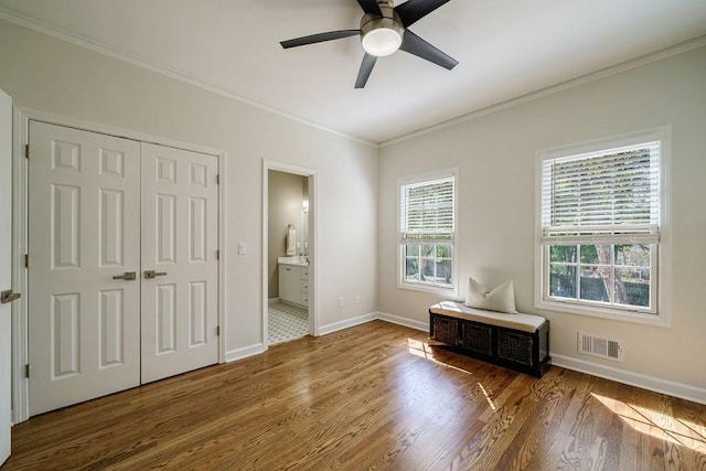 unfurnished bedroom with ceiling fan, ensuite bathroom, crown molding, wood-type flooring, and a closet