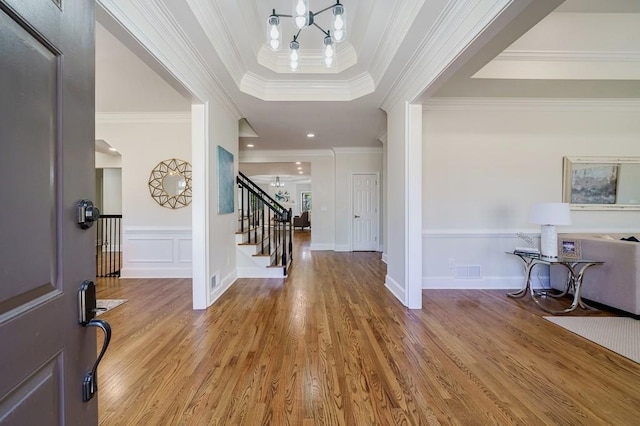 entryway with hardwood / wood-style flooring, ornamental molding, and a notable chandelier