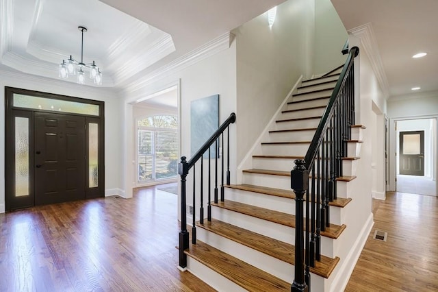 entryway with a raised ceiling, wood-type flooring, crown molding, and a chandelier