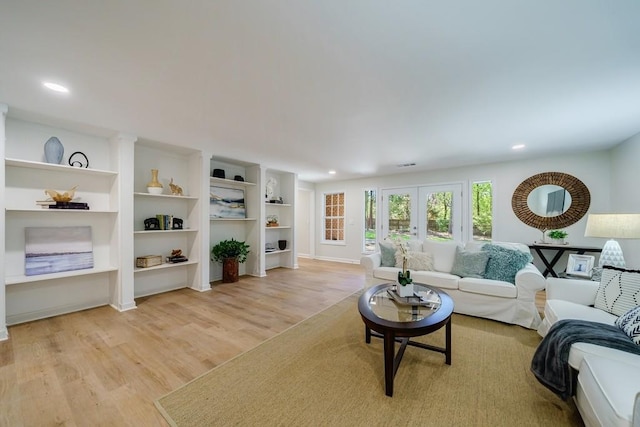 living room with built in features, light hardwood / wood-style flooring, and french doors